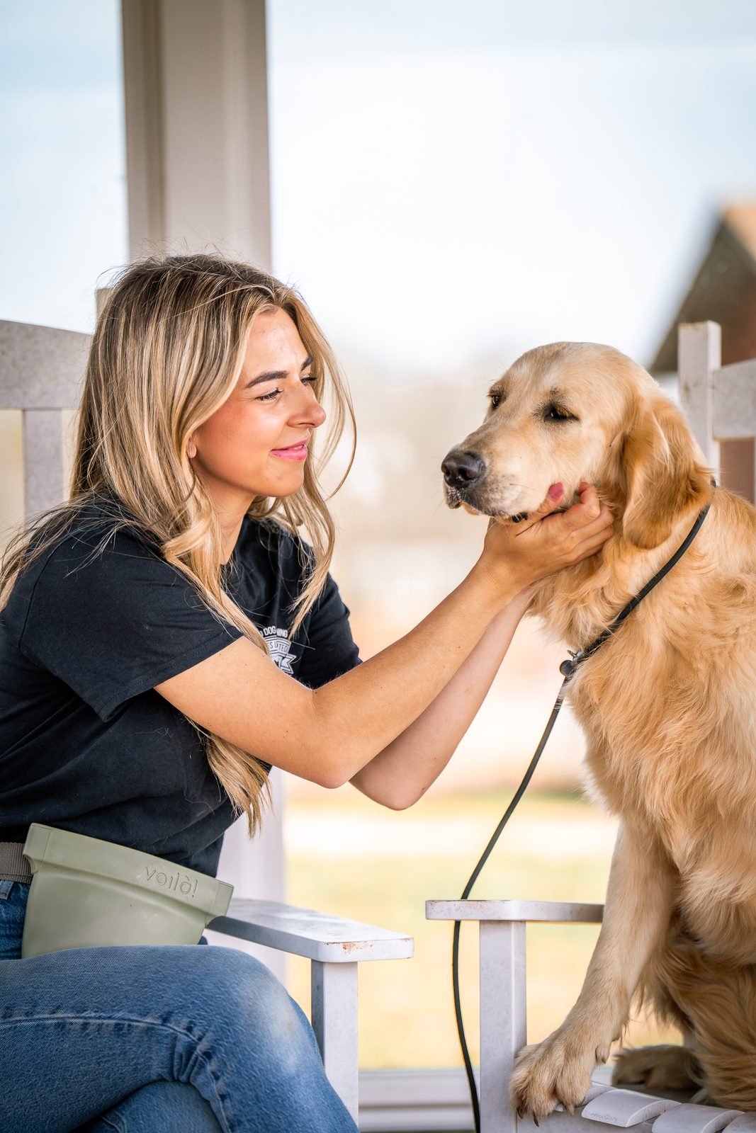A woman petting the face of a golden retriever in the sun on a porch