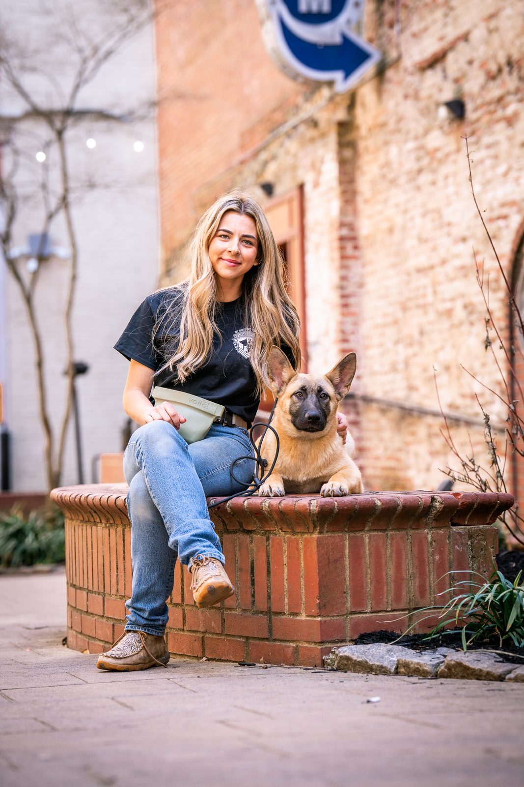 A woman on a brick planter and a young Malinois sitting alongside