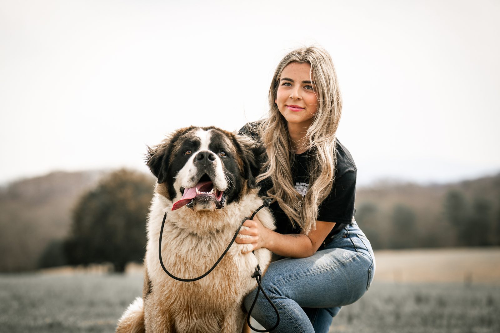 A woman with an arm around a smiling Saint Bernard on a hill