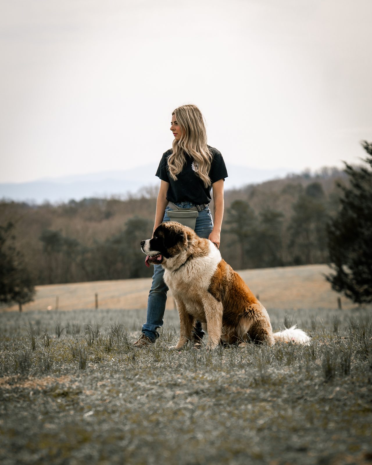 A woman looking to one side while a Saint Bernard sits at her hip
